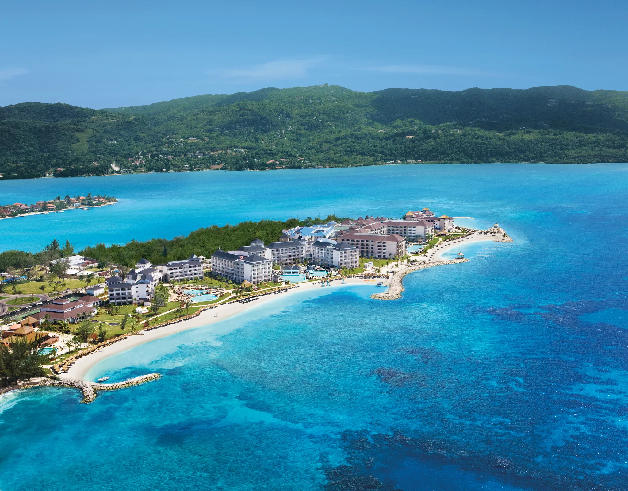 Aerial view of Secrets Wild Orchid Montego Bay overlooking turquoise lagoon waters and surrounding hills in Jamaica.