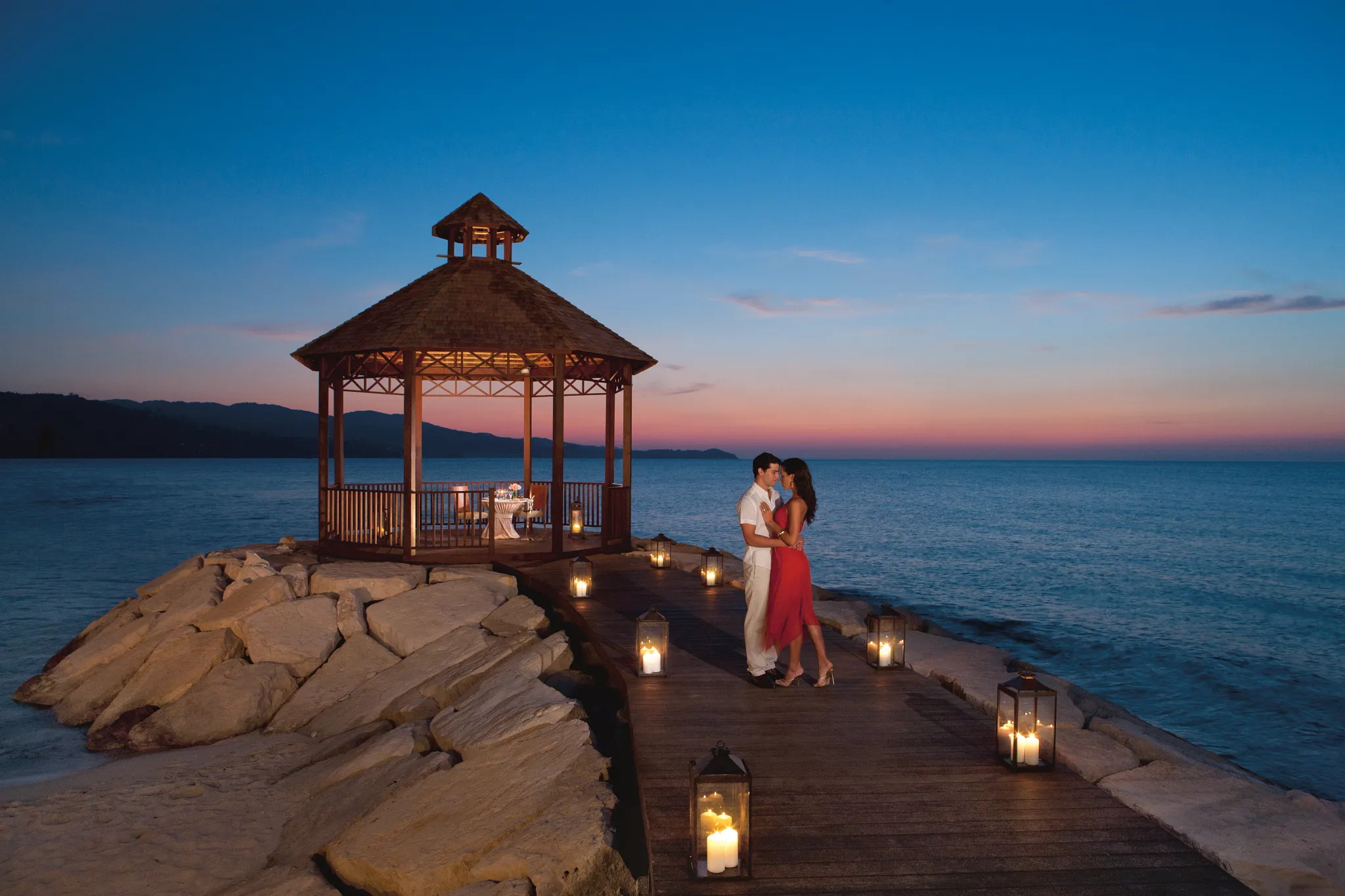 Couple enjoying a romantic candlelit dinner at a seaside gazebo at Secrets Wild Orchid Montego Bay at sunset.