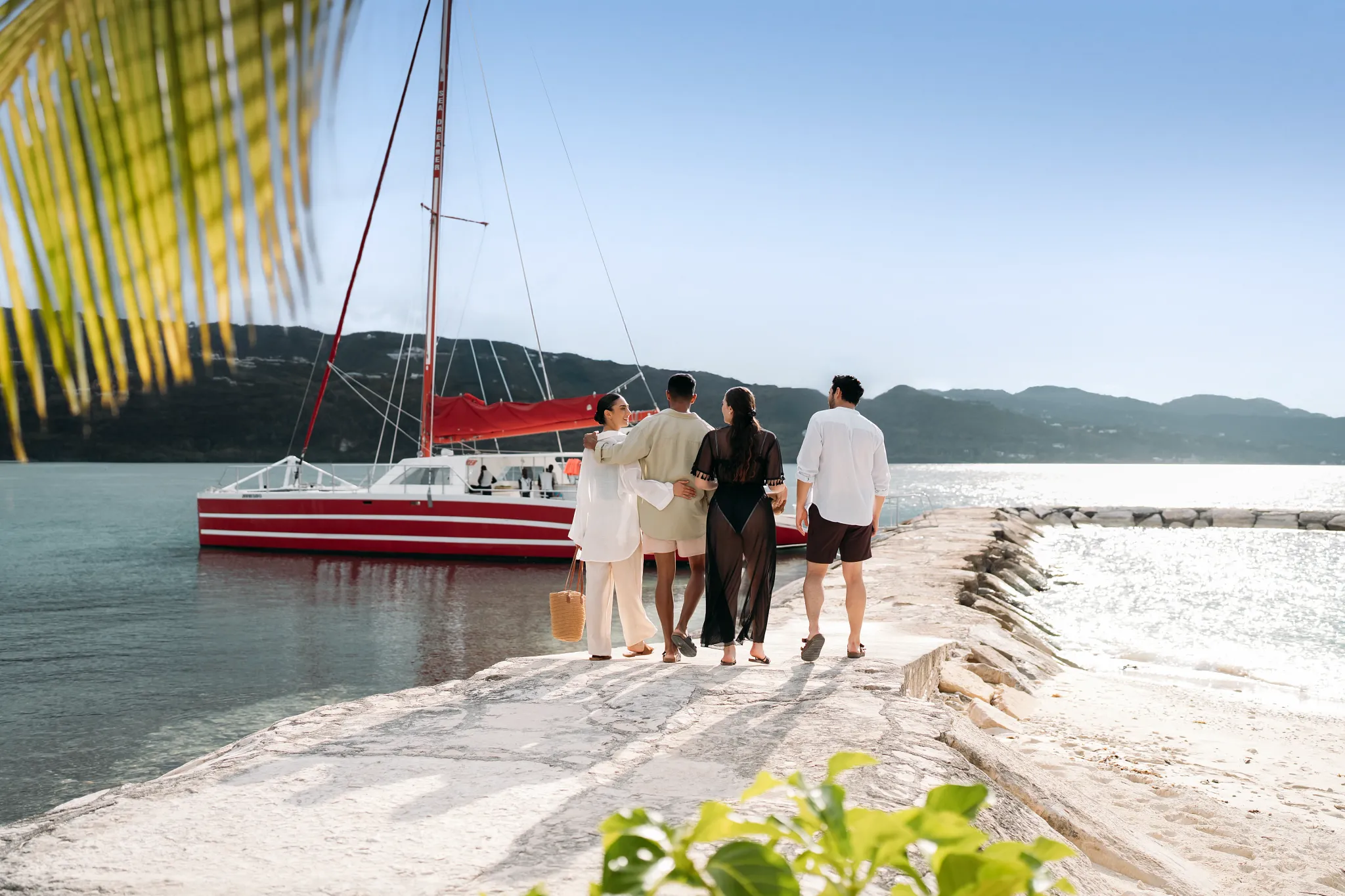 Couples walking toward a red catamaran for a sunset cruise near Secrets Wild Orchid Montego Bay.